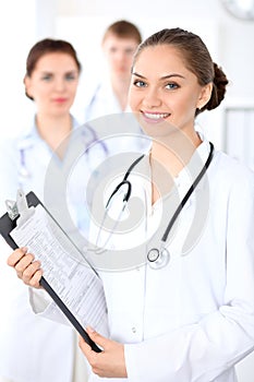 Happy female doctor keeping medical clipboard while medical staff are at the background