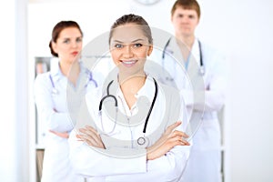 Happy female doctor keeping medical clipboard while medical staff are at the background