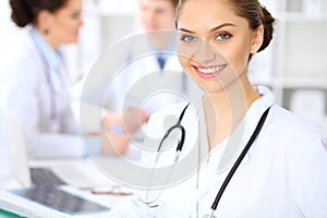 Happy female doctor keeping medical clipboard while medical staff are at the background