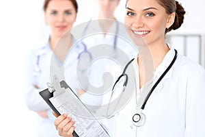 Happy female doctor keeping medical clipboard while medical staff are at the background