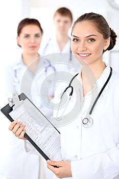 Happy female doctor keeping medical clipboard while medical staff are at the background