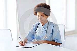 Happy female doctor or nurse writing to clipboard