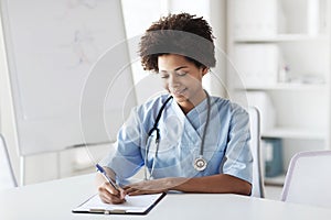 Happy female doctor or nurse writing to clipboard