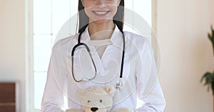 Happy female doctor paediatrician holding teddy bear look at camera