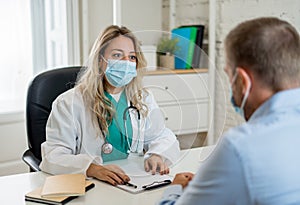 Happy female doctor and patient wearing protective face mask having a consultation in clinic office