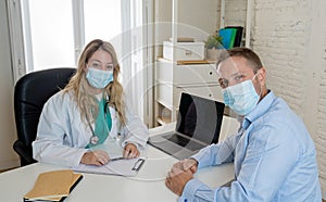 Happy female doctor and patient wearing protective face mask having a consultation in clinic office