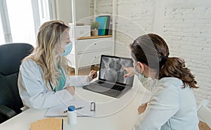 Happy female doctor and patient wearing protective face mask having a consultation in clinic office