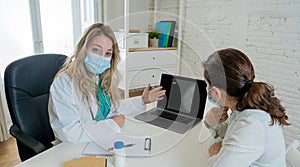 Happy female doctor and patient wearing protective face mask having a consultation in clinic office