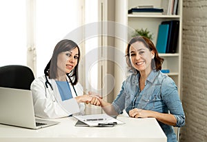 Happy female doctor and young smiling woman patient shaking hands in clinic office