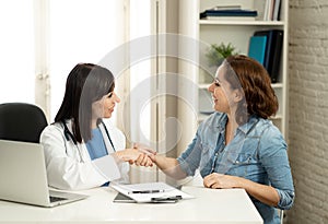 Happy female doctor and young smiling woman patient shaking hands in clinic office