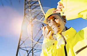 Happy female Electrical engineer talking in a walkie talkie to control a high voltage electricity pylon. Electrical power lines