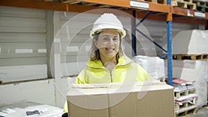 Happy female employee holding cardboard box in warehouse.