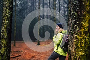 Happy female excursionist enjoy nature background and forest around smiling and resting against a tree. Travel backpacker woman in photo