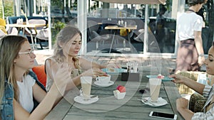 Happy female friends enjoying lunch in outdoor cafe while waitress bringing desserts on summer day