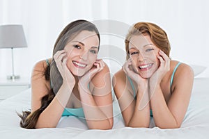 Happy female friends in teal tank tops lying in bed