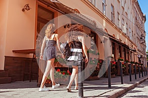 Happy female friends walking along old city streets in summer. Back view