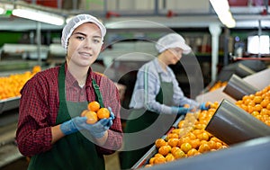 Happy female fruit sorting factory worker holding tangerines