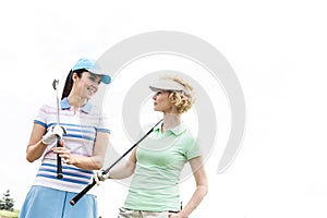 Happy female golfers looking at each other against clear sky