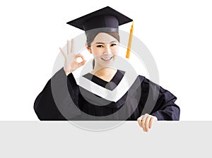 Happy female graduate showing blank board with ok gesture