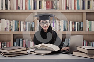 Happy female graduate study at library with laptop