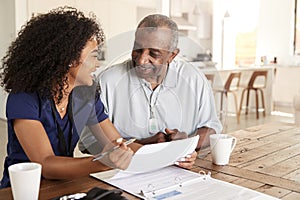 Happy female healthcare worker sitting at table smiling with a senior man during a home health visit photo