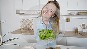 Happy female housewife takes bunch of salad leaves in hands and