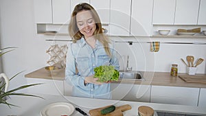 Happy female housewife takes bunch of salad leaves in hands and