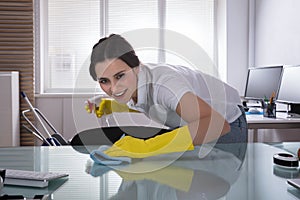 Happy Female Janitor Cleaning Desk With Rag