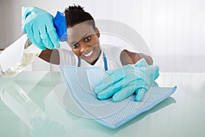 Happy Female Janitor Cleaning Desk With Rag