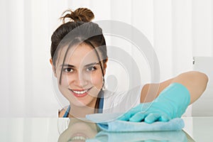 Happy Female Janitor Cleaning Desk With Rag