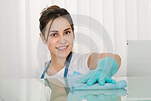 Happy Female Janitor Cleaning Desk With Rag