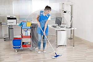 Happy Female Janitor Mopping Floor In Office