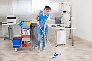 Happy Female Janitor Mopping Floor In Office photo