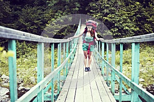 Happy female mountaineer standing on a wooden bridge over a mountain stream overflowing with excitement with the glory and beauty