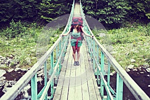 Happy female mountaineer standing on a wooden bridge over a mountain stream overflowing with excitement with the glory and beauty