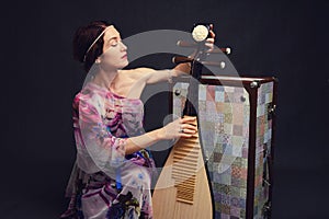 A happy female musician in Asian clothes on a studio black backgroun