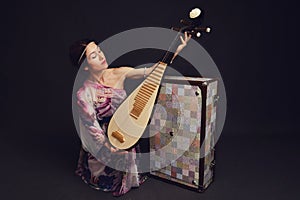 A happy female musician in Asian clothes on a studio black backgroun