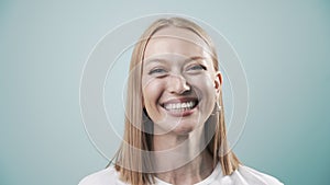 Happy female with natural white teeth laughing to camera, selective focus. Smiling woman face with perfect smile in light blue