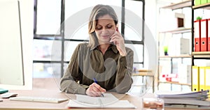 Happy female office worker making phone call, smiling, listening to conversation and making notes