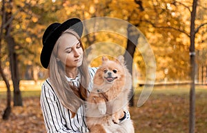 Happy female owner with her dog on hands, arms. Young woman hugging her miniature fluffy Pomeranian Spitz puppy outdoor