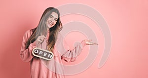 Happy female owner holding open sign and gesturing in pink studio