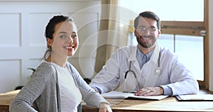 Happy female patient sitting at table with smiling general practitioner.