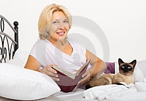 Happy female pensioner with cat reading book