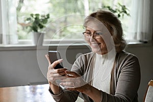 Happy female pensioner holding mobile phone enjoy using web app