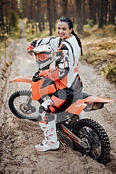 Happy female racer wearing motorcycle outfit sitting on her bike off-road in the woods