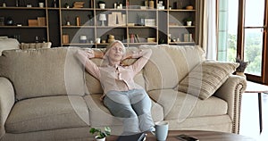 Happy female retiree enjoy peaceful moment relax on cozy couch