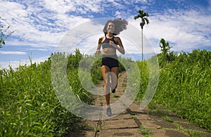 Happy female runner training on countryside road - young attractive and fit jogger woman doing running workout outdoors at
