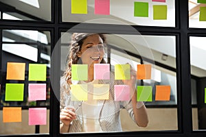 Happy female scrum master writing tasks on sticky paper notes. photo