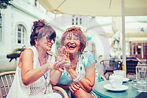 Happy female senior friends laughing and pointing fingers to someone while drinking coffee