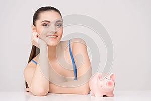 Happy female sitting at table with piggy bank. photo